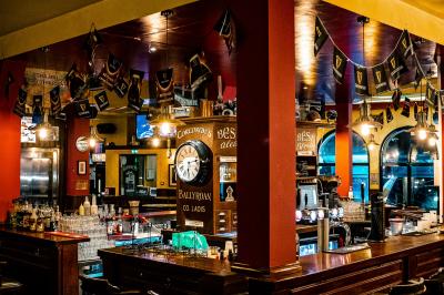 Façade d'un pub irlandais avec enseignes vertes, drapeau irlandais et arbres aux feuilles d'automne.