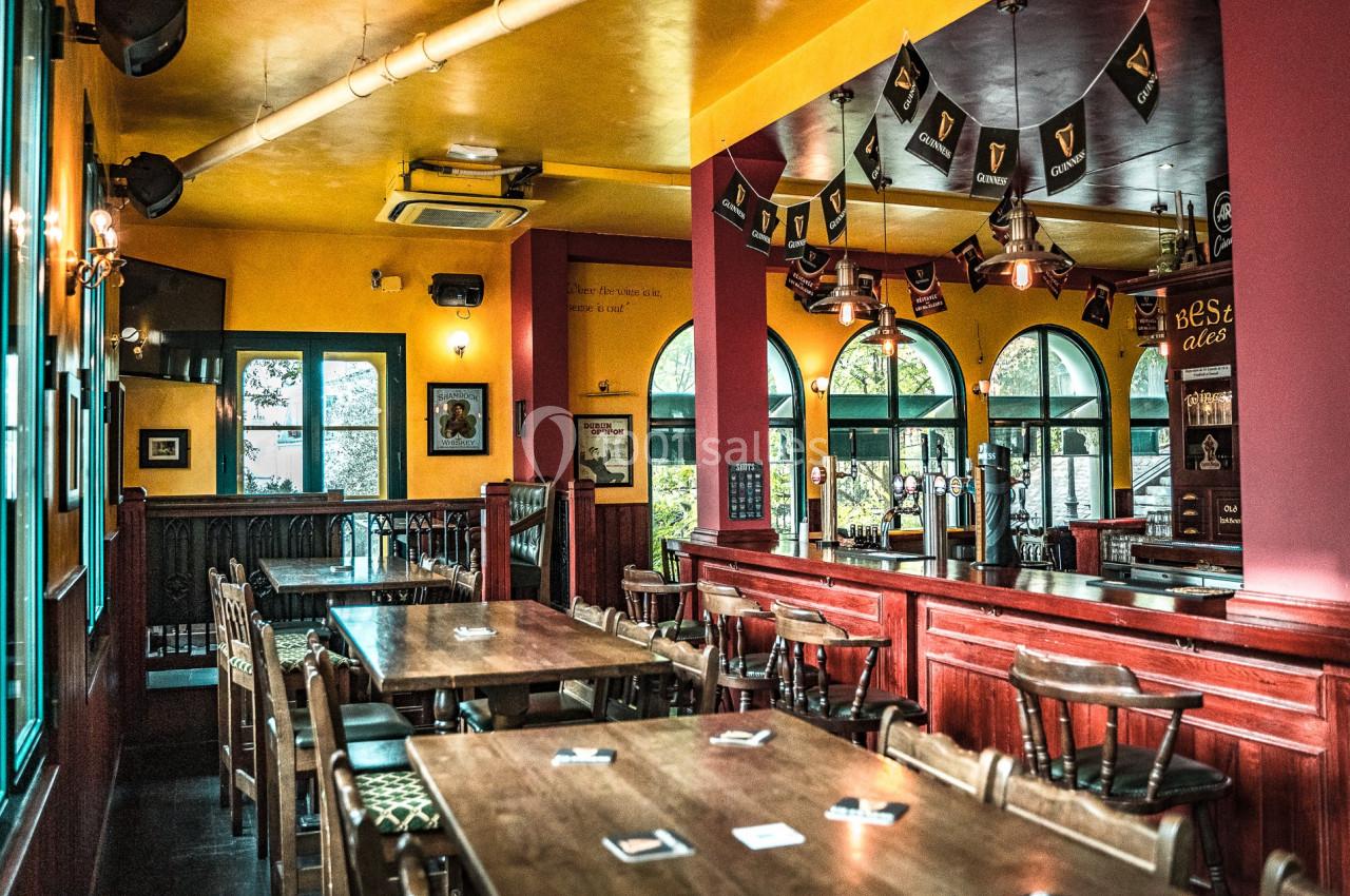 Intérieur d'un pub chaleureux avec des tables en bois, des chaises, des décorations et des drapeaux suspendus.