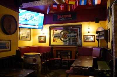 Intérieur d'un pub avec des tables en bois, des tabourets, un tableau noir et une ambiance tamisée.
