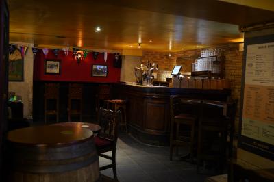 Intérieur d'un pub avec des tables en bois, des tabourets, un tableau noir et une ambiance tamisée.