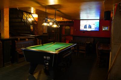 Intérieur d'un pub avec des tables en bois, des tabourets, un tableau noir et une ambiance tamisée.