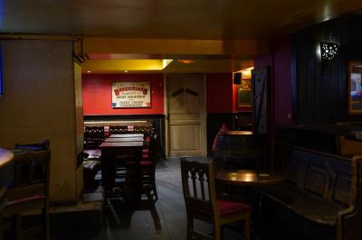Intérieur d'un pub avec des tables en bois, des tabourets, un tableau noir et une ambiance tamisée.