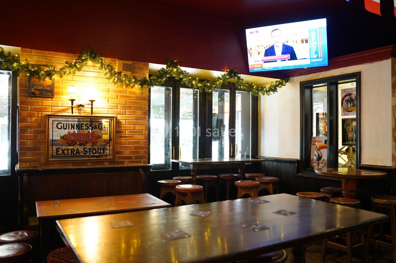 Intérieur d'un pub avec des tables en bois, des tabourets, des guirlandes lumineuses et une télévision diffusant des…