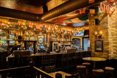 Intérieur d'un pub avec des tables en bois, des tabourets, un tableau noir et une ambiance tamisée.