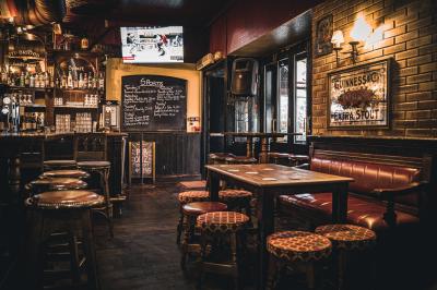 Intérieur d'un pub avec des tables en bois, des tabourets, un tableau noir et une ambiance tamisée.