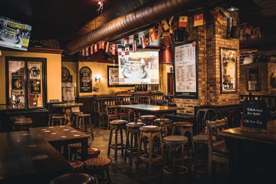 Intérieur d'un pub avec des tables en bois, des tabourets, un tableau noir et une ambiance tamisée.