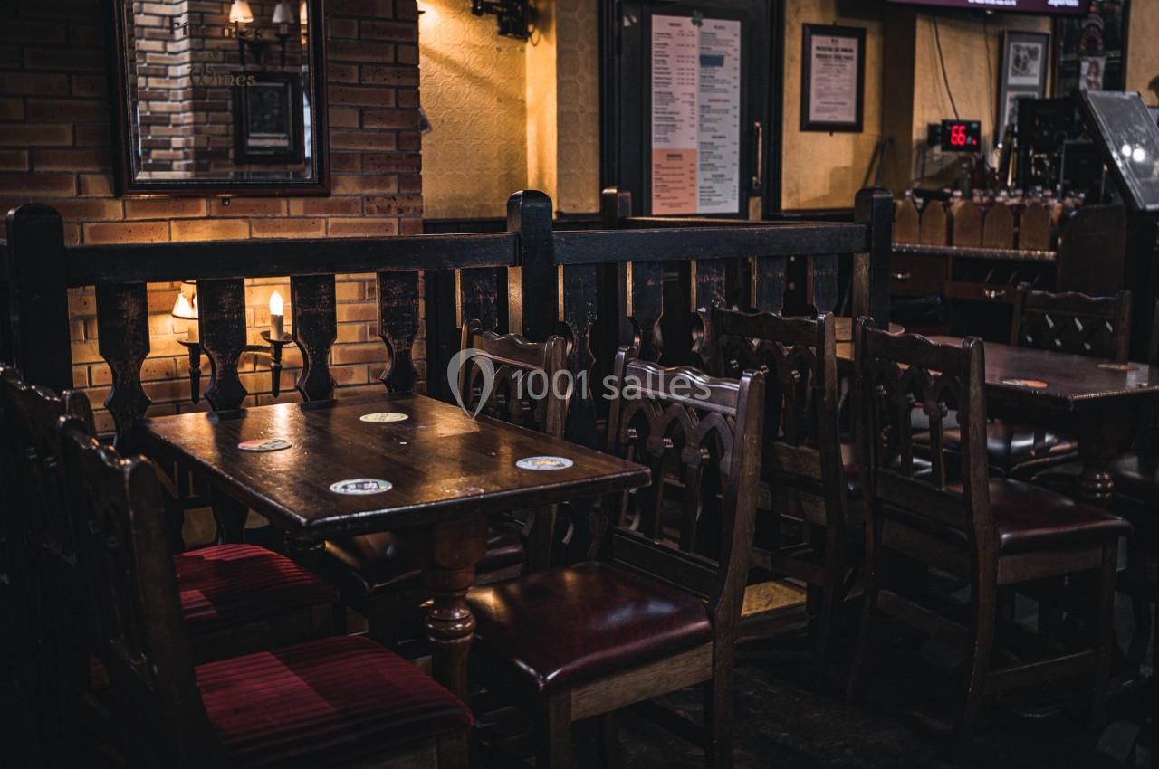 Salle d’un pub avec des tables en bois, des chaises rembourrées et une ambiance tamisée.