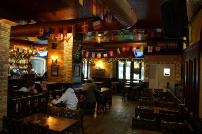 Intérieur d'un pub avec des tables en bois, des tabourets, un tableau noir et une ambiance tamisée.