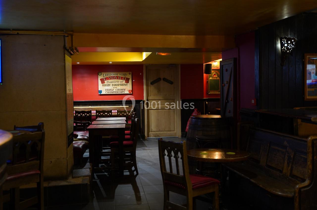 Intérieur d'un pub avec des tables en bois, des chaises rembourrées rouges et un éclairage tamisé.