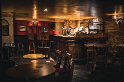 Intérieur d'un pub avec des tables en bois, des tabourets, un tableau noir et une ambiance tamisée.
