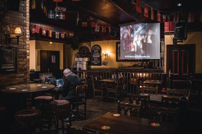 Intérieur d'un pub avec des tables en bois, des tabourets, un tableau noir et une ambiance tamisée.