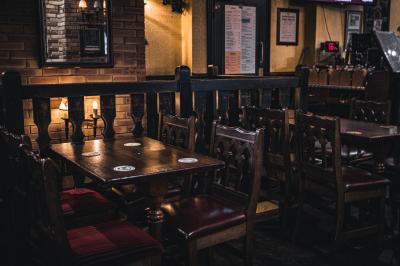 Intérieur d'un pub avec des tables en bois, des tabourets, un tableau noir et une ambiance tamisée.