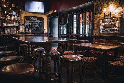 Intérieur d'un pub avec des tables en bois, des tabourets, un tableau noir et une ambiance tamisée.