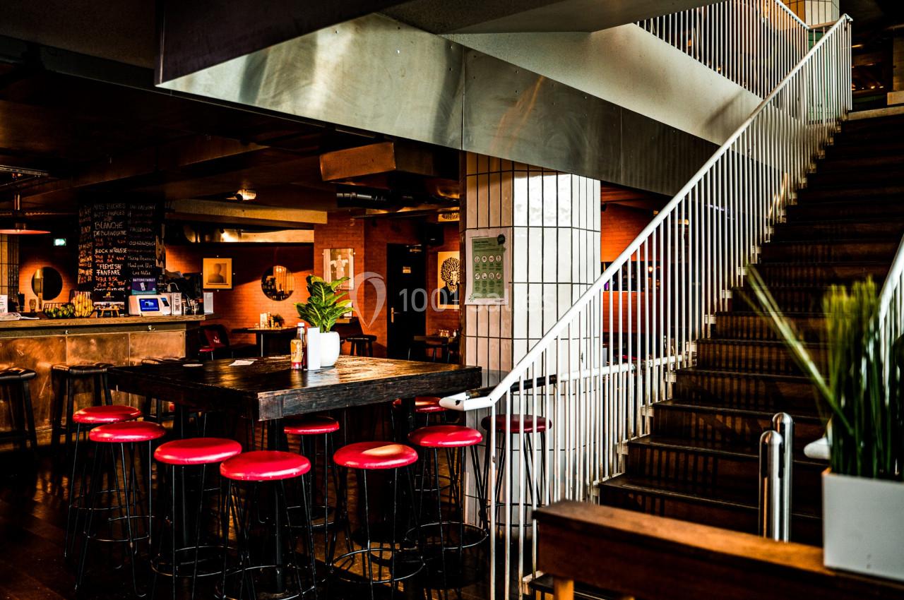 Intérieur d'un café moderne avec tabourets rouges, table haute en bois et escalier en métal.