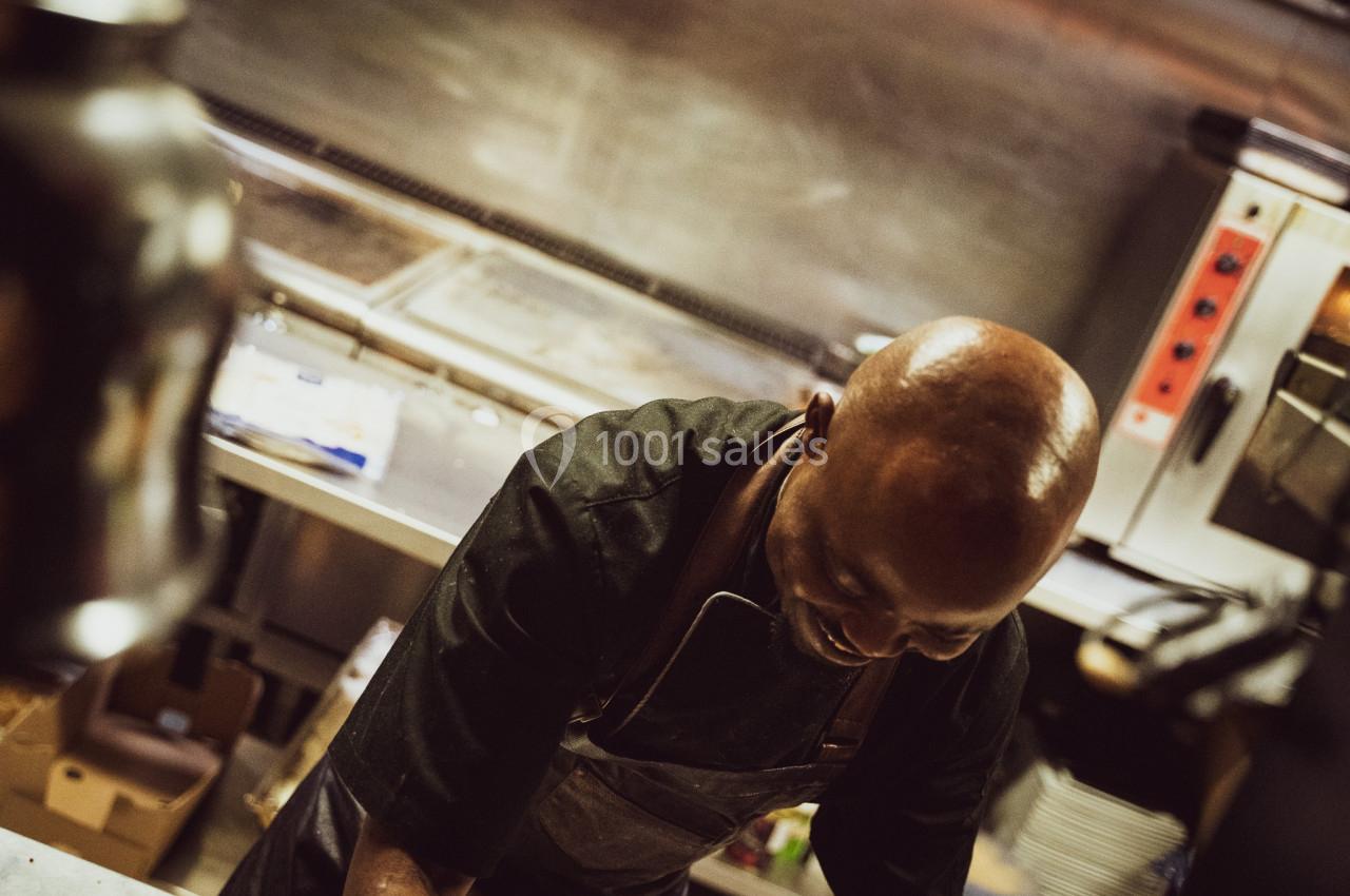 Un chef cuisinier en tablier noir travaille dans une cuisine professionnelle.