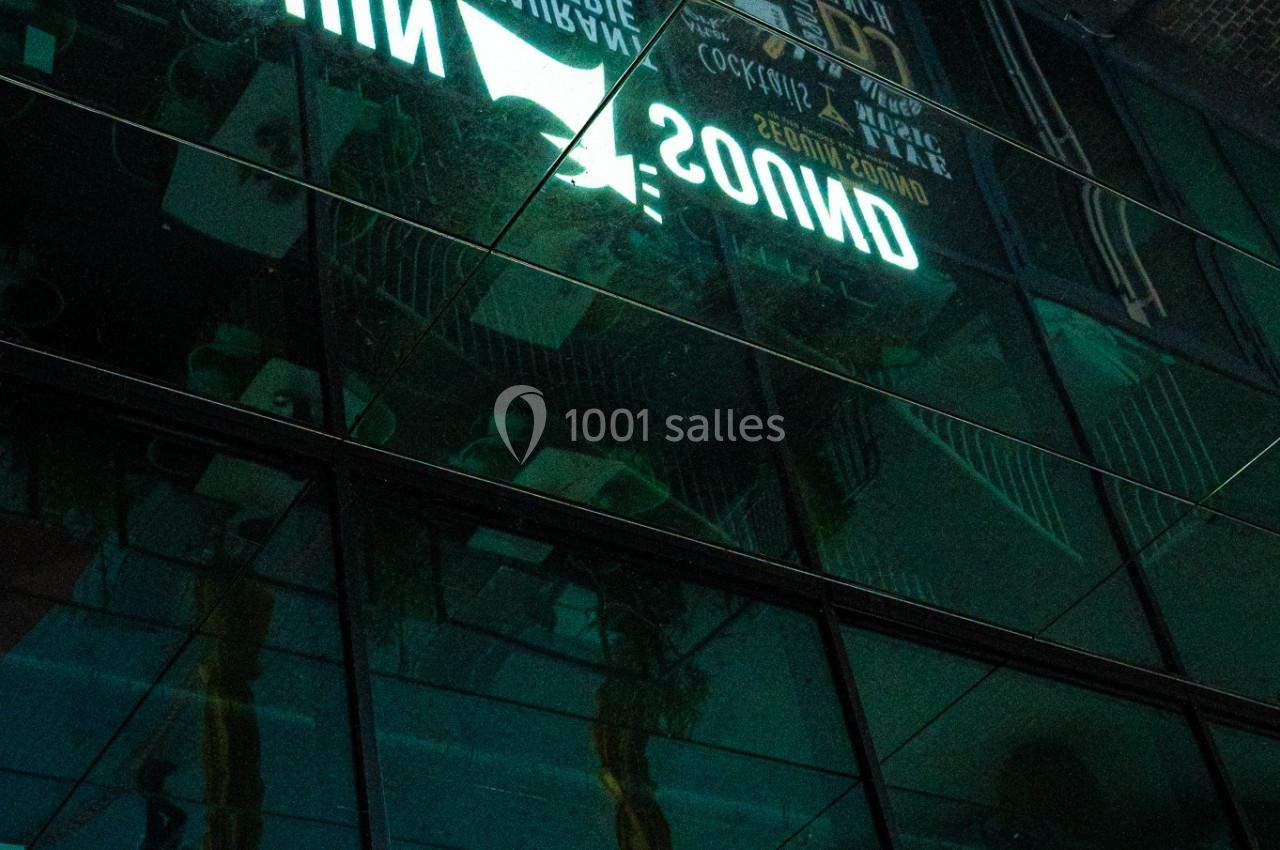 Reflet d'une enseigne lumineuse ’Seguin Sound’ sur une façade vitrée, avec des éléments urbains en arrière-plan.