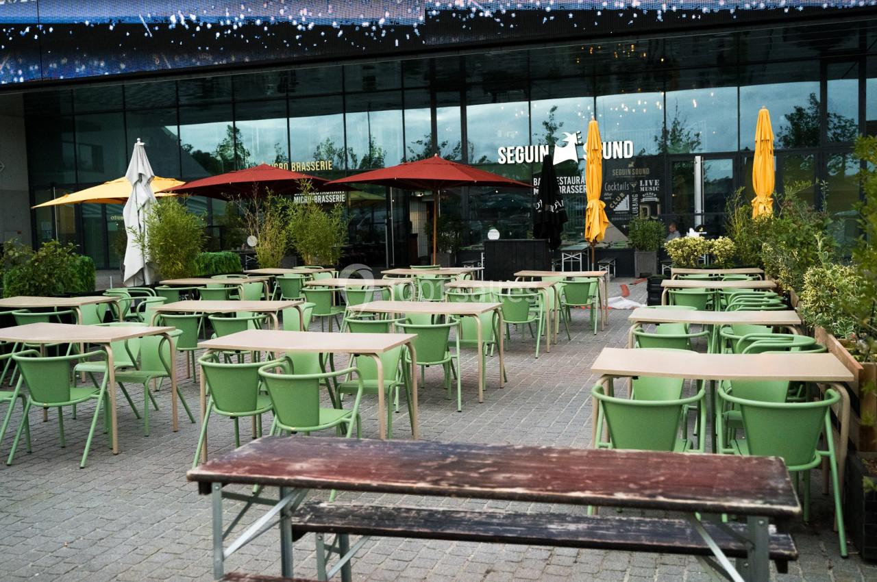 Terrasse d'un café-restaurant avec des tables et chaises vertes, entourée de parasols colorés et de plantes.