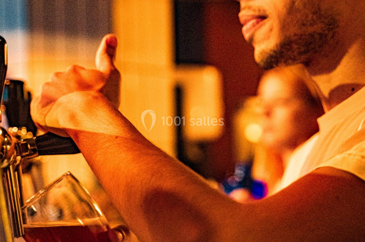 Un homme sert une bière pression dans un verre transparent dans un environnement faiblement éclairé.