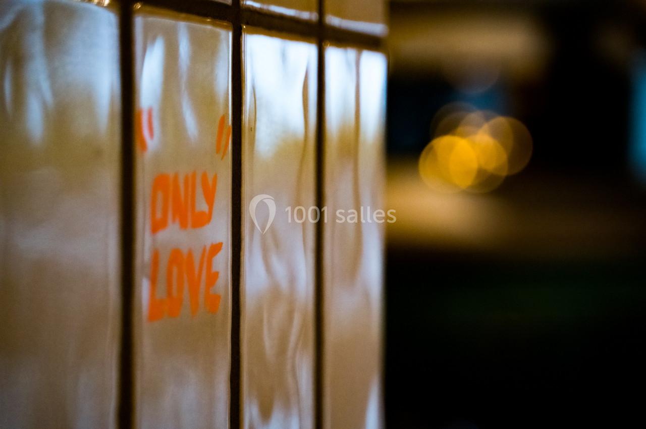 Texte ’Only Love’ peint en rouge sur un mur carrelé, avec un arrière-plan flou et des lumières urbaines.