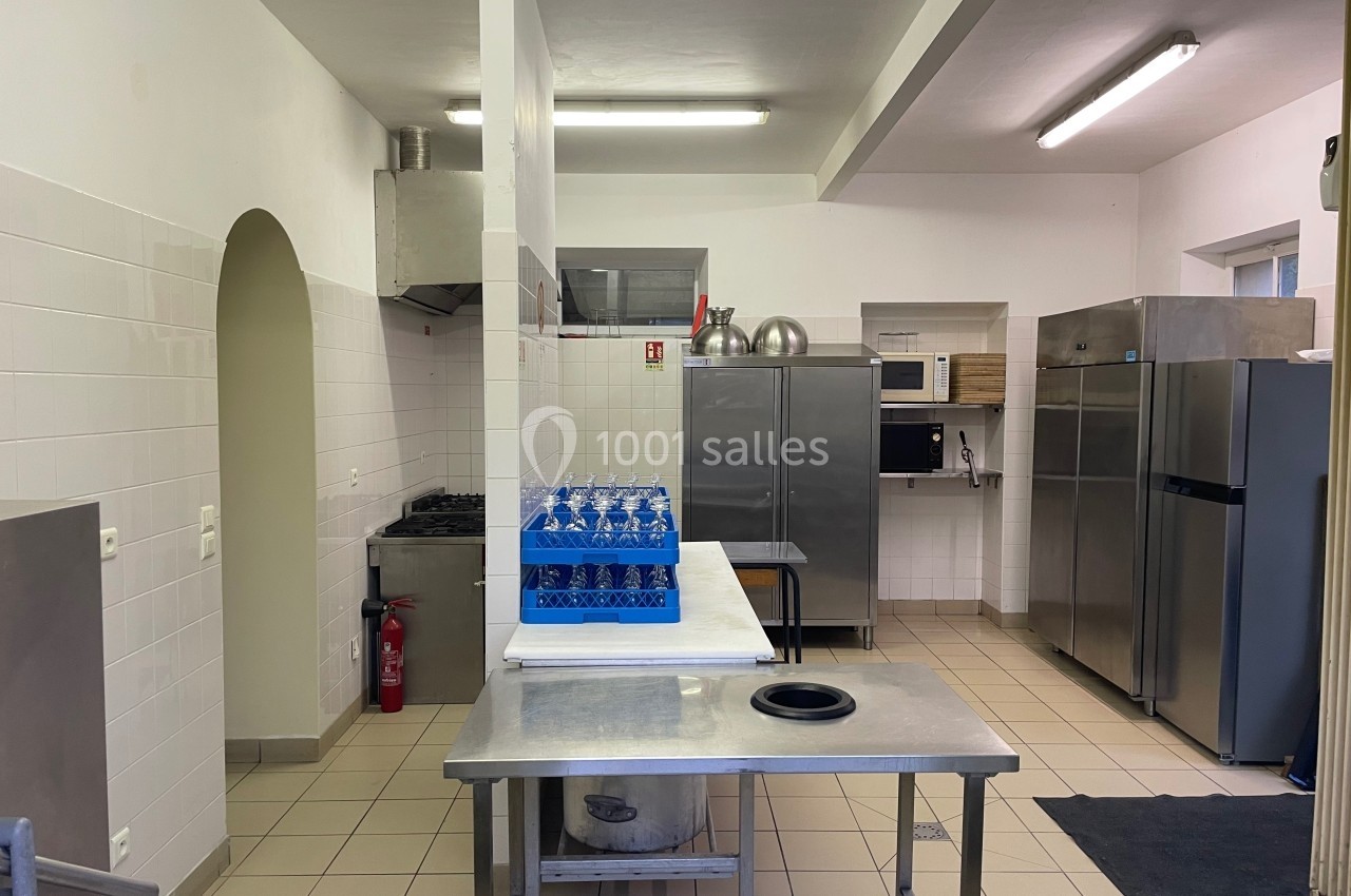 Cuisine professionnelle avec plans de travail en inox, réfrigérateurs, four, micro-ondes et carafe d'eau alignée.
