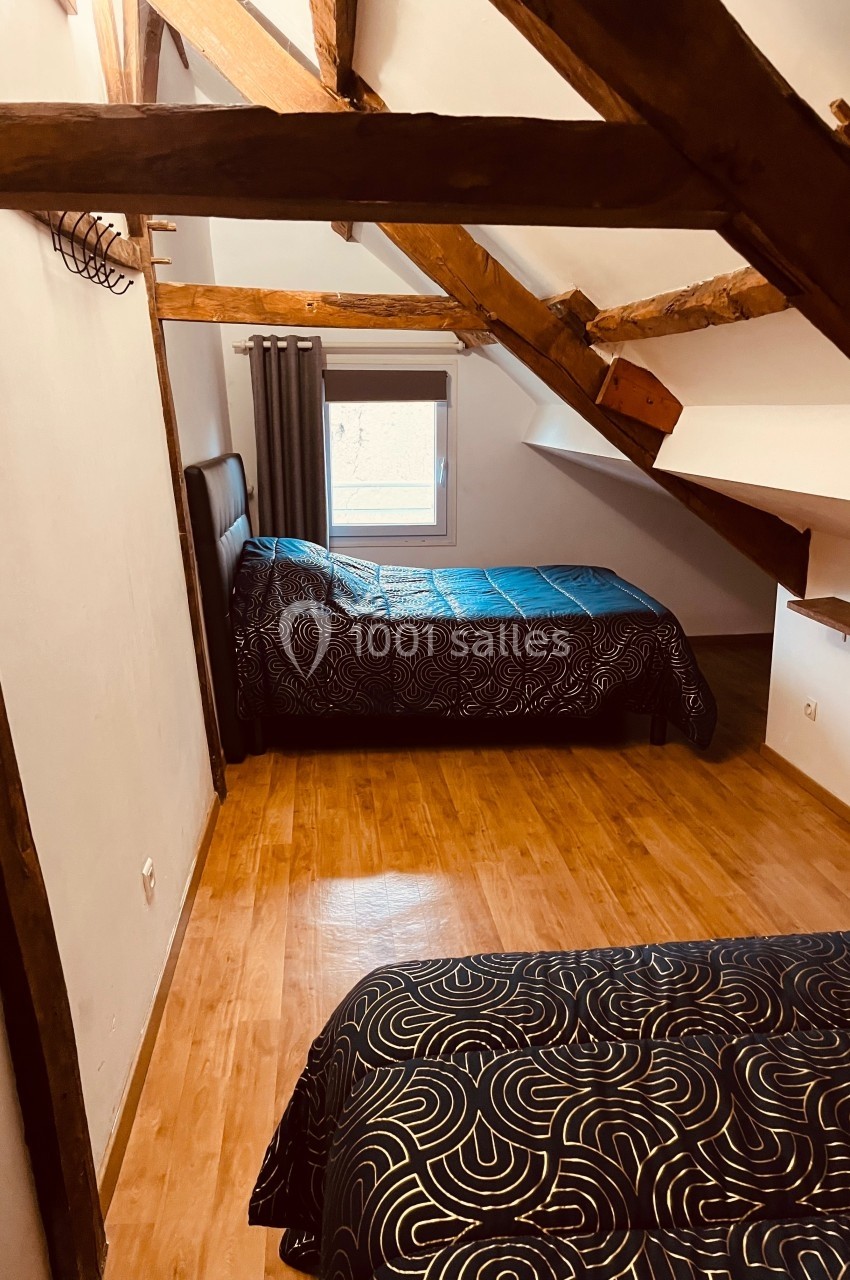 Chambre mansardée avec parquet, deux lits simples et une fenêtre apportant de la lumière naturelle.