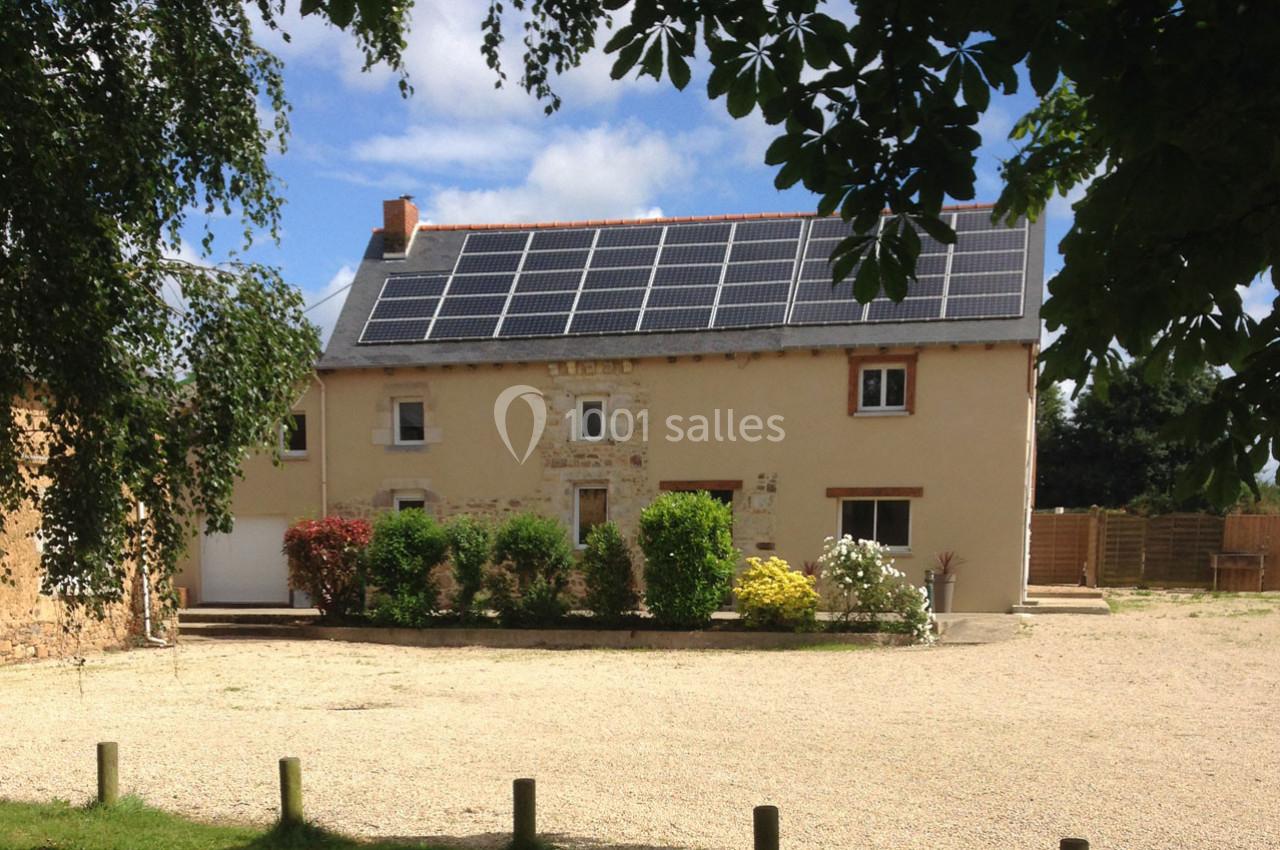 Maison en pierre rénovée avec panneaux solaires sur le toit, entourée d'arbres et d'un jardin avec allée gravillonnée.