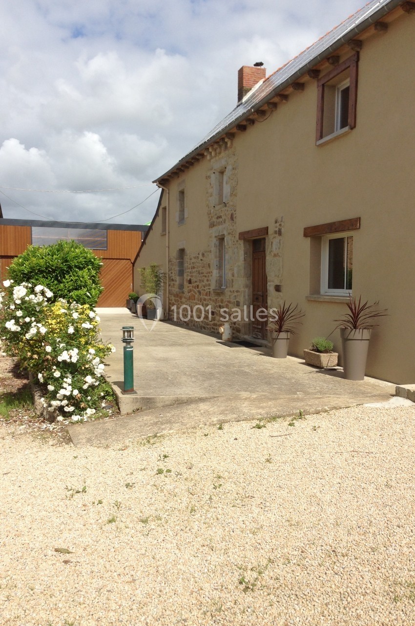 Façade d'une maison en pierre rénovée avec des jardinières, une allée en gravier et un portail en bois au fond.