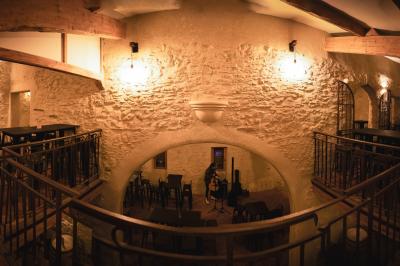 Salle rustique avec murs en pierre, tonneaux en bois servant de tables, tabourets métalliques et éclairage chaleureux.