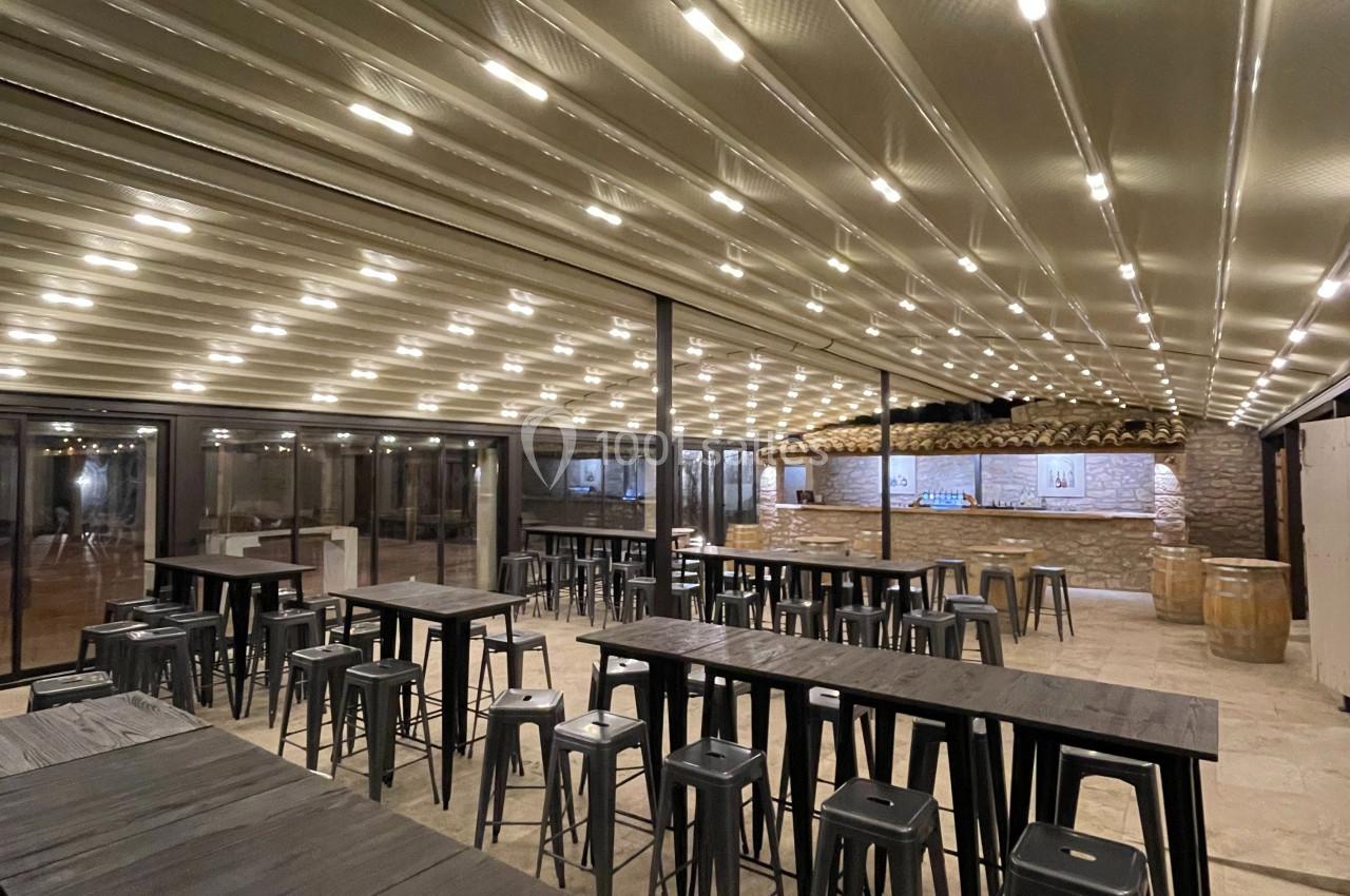 Salle spacieuse avec de longues tables en bois, chaises hautes et plafond éclairé par des rangées de lumières intégrées.