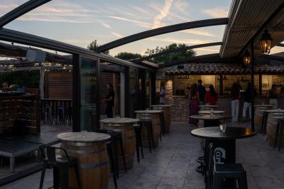 Salle rustique avec murs en pierre, tonneaux en bois servant de tables, tabourets métalliques et éclairage chaleureux.