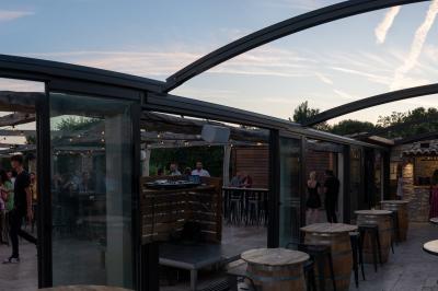 Salle rustique avec murs en pierre, tonneaux en bois servant de tables, tabourets métalliques et éclairage chaleureux.