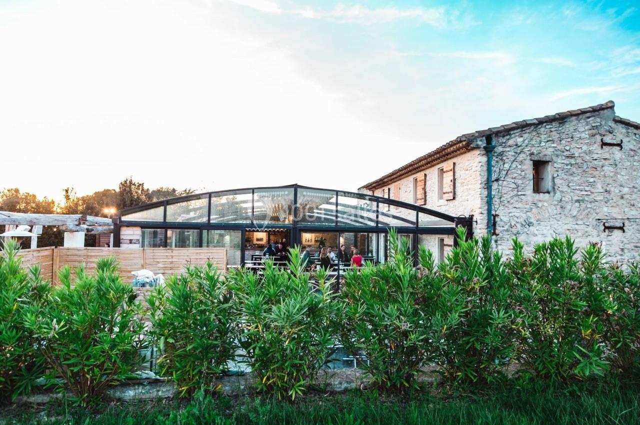 Bâtiment en pierre avec une verrière moderne entourée de végétation sous un ciel dégagé.