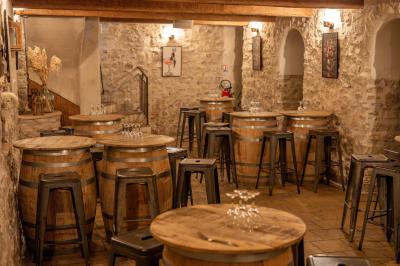 Salle rustique avec murs en pierre, tonneaux en bois servant de tables, tabourets métalliques et éclairage chaleureux.