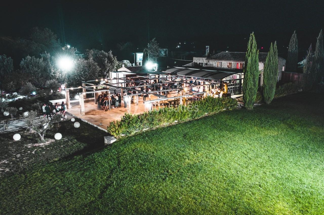 Vue aérienne nocturne d'un espace événementiel éclairé avec terrasse et pelouse environnante.