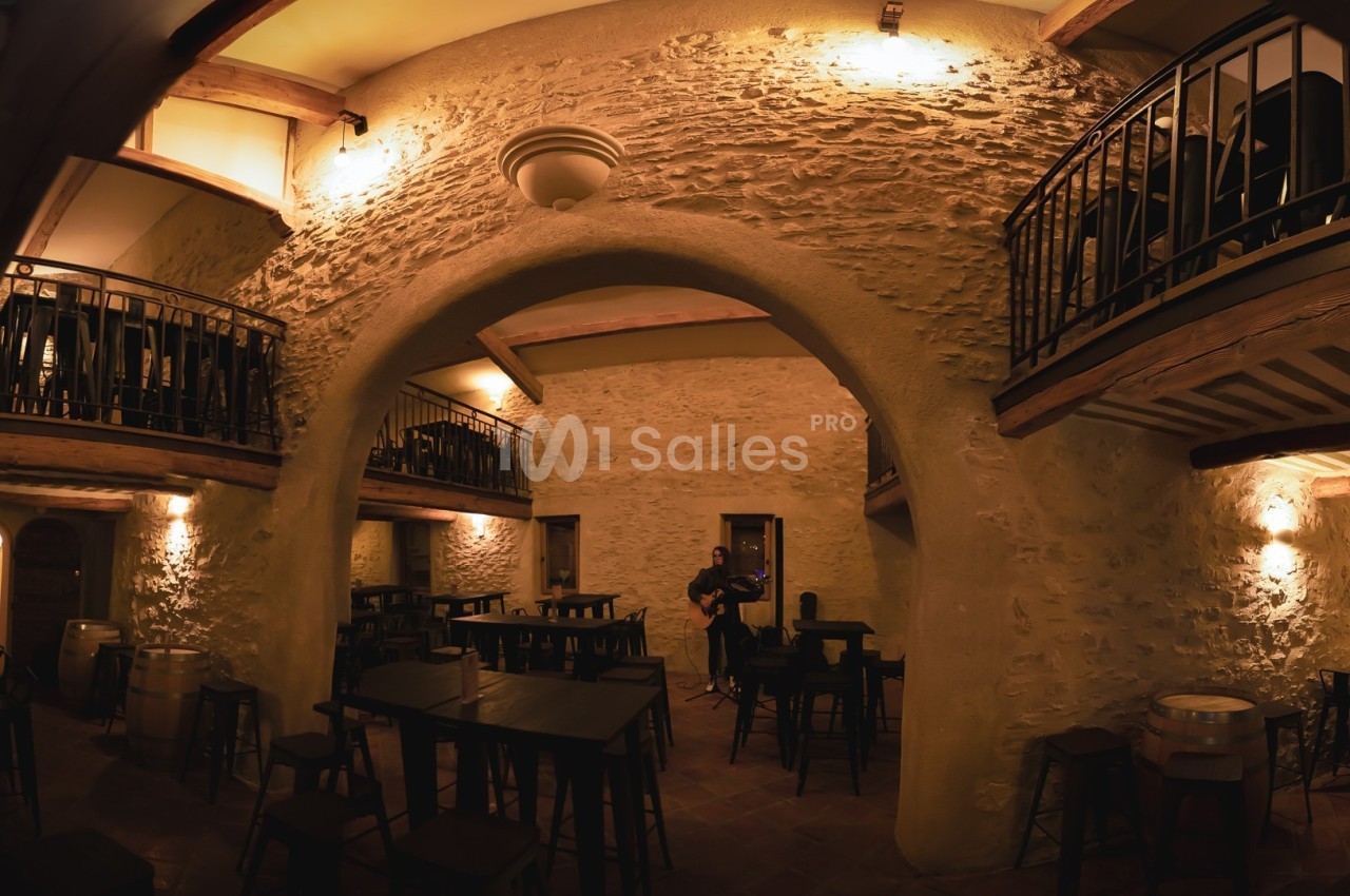 Salle intérieure en pierre avec tables, chaises, mezzanines en bois et éclairage tamisé.
