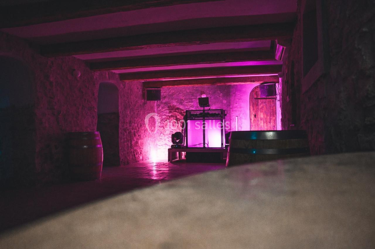 Salle en pierre avec éclairage rose, tonneaux en bois et équipement lumineux au fond.