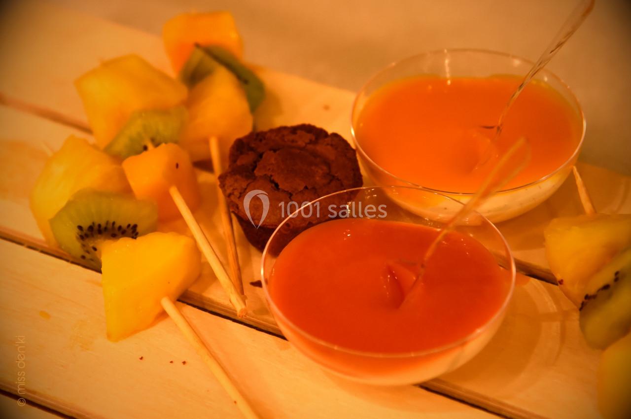 Brochettes de fruits frais avec deux sauces colorées et un petit gâteau au chocolat sur une table en bois clair.