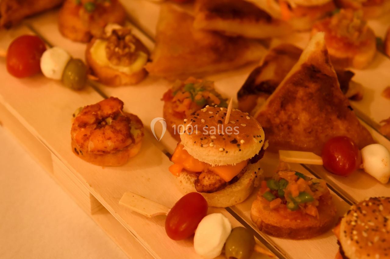 Assortiment de bouchées apéritives variées disposées sur un plateau en bois, incluant mini-burgers, feuilletés et brochettes.