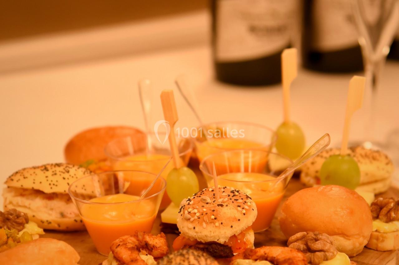 Plateau en bois avec amuse-bouches variés, mini-sandwichs, verrines et brochettes, deux bouteilles en arrière-plan.