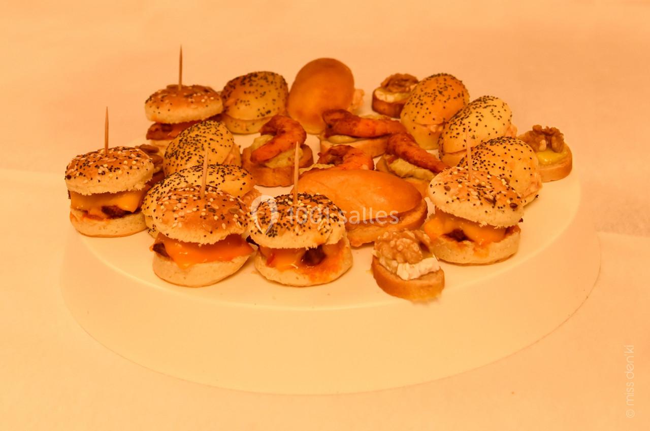 Plateau de mini-burgers, bouchées salées et amuse-bouches variés disposés sur un support blanc.