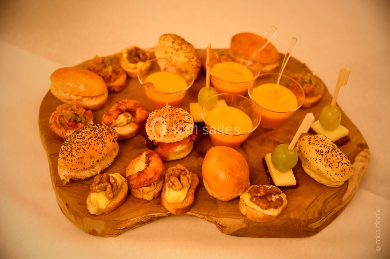 Plateau de bouchées apéritives variées comprenant mini-burgers, verrines, fruits et amuse-bouches sur planche en bois.