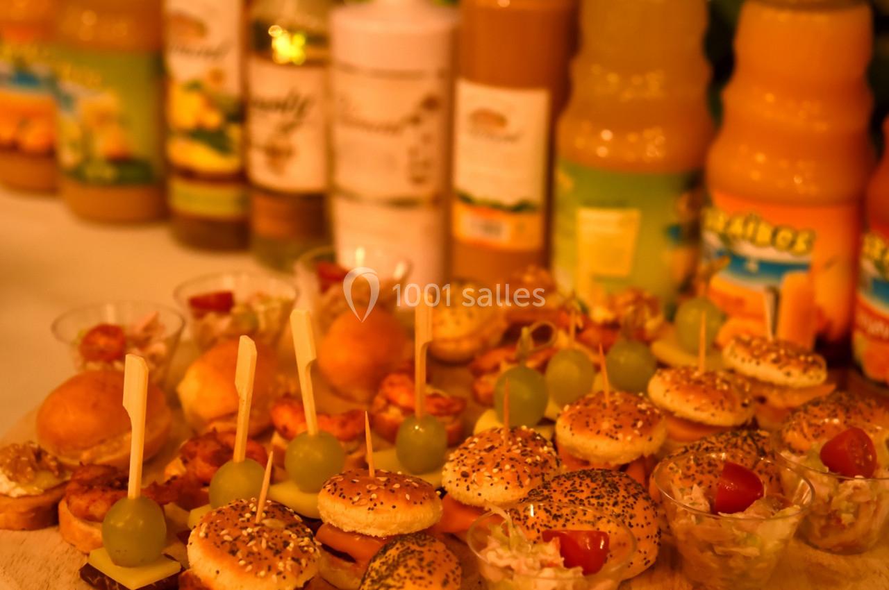 Plateau de mini-burgers, verrines et amuse-bouches disposés devant des bouteilles de jus de fruits variés.