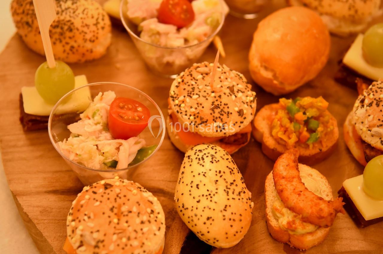 Plateau en bois avec un assortiment de bouchées apéritives, incluant mini-burgers, verrines et amuse-bouches variés.