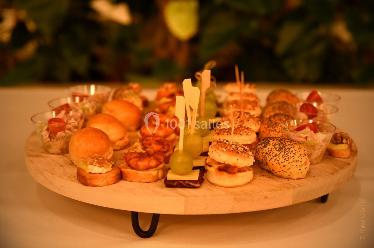 Plateau en bois garni de bouchées variées, incluant mini-burgers, brochettes et verrines, présenté sur une table.