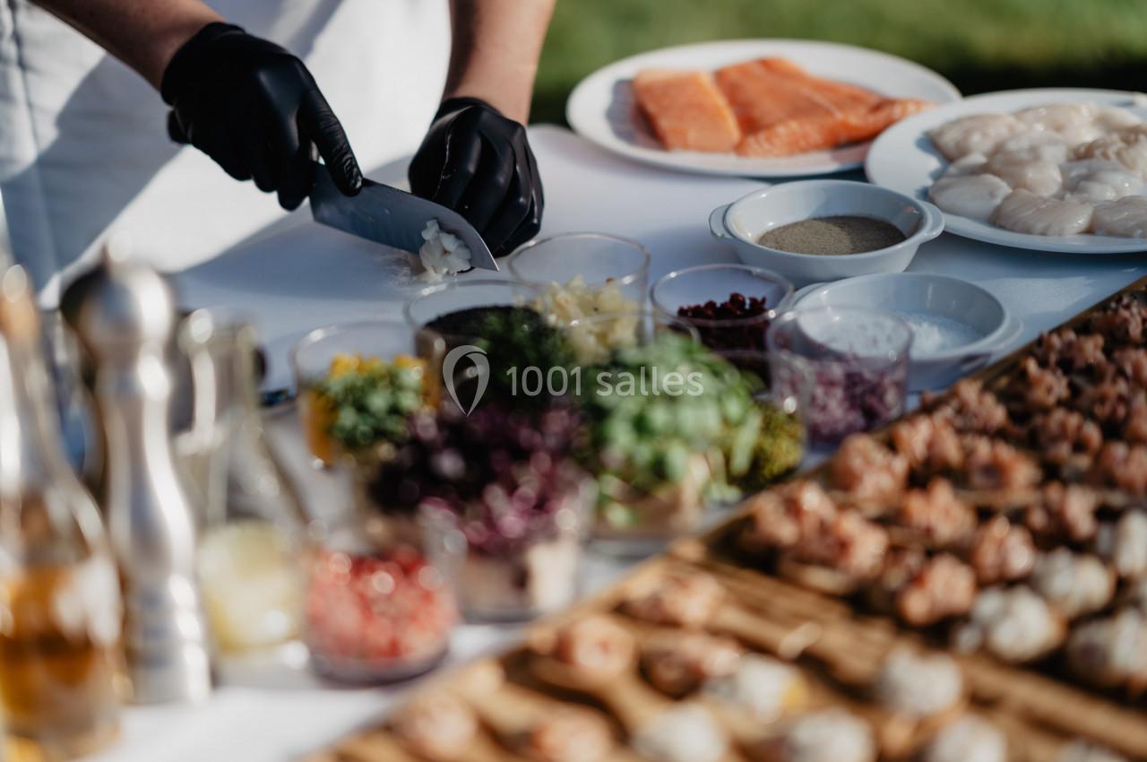 Un chef découpe des oignons sur une table garnie d'ingrédients frais, de poissons et de fruits de mer.