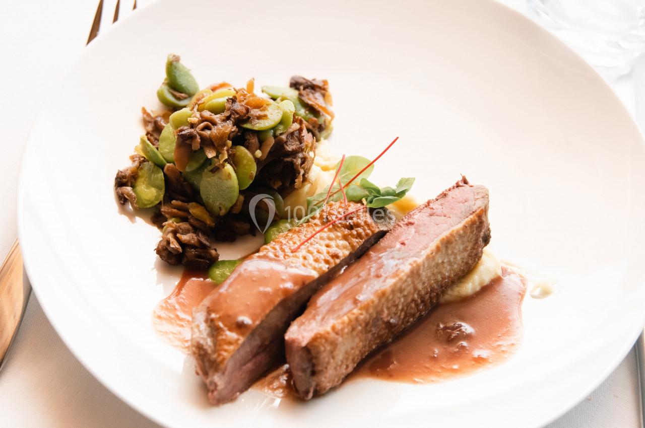 Assiette contenant du magret de canard nappé de sauce, accompagné de légumes sautés et d'une purée.