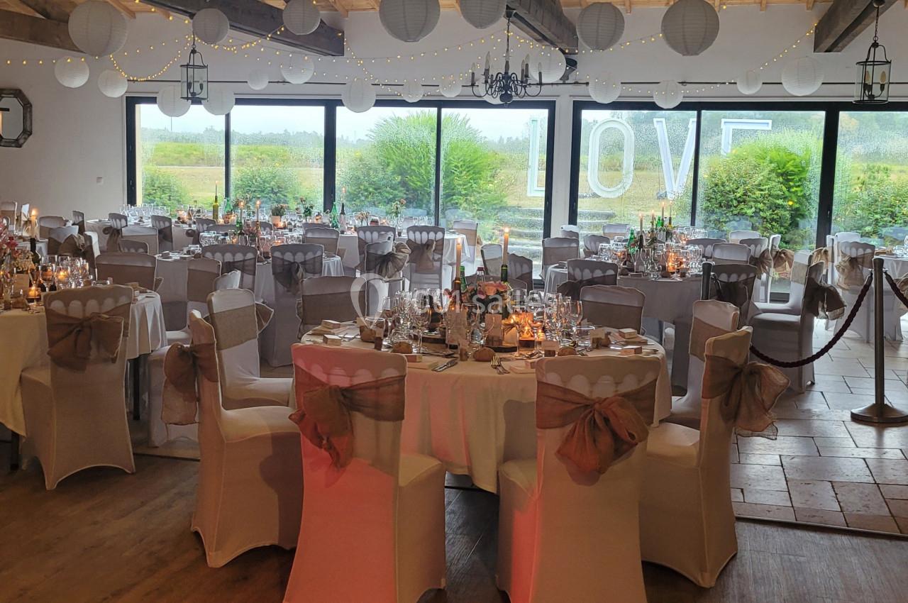 Salle de réception décorée pour un mariage, avec tables dressées, guirlandes lumineuses et vue sur un jardin.