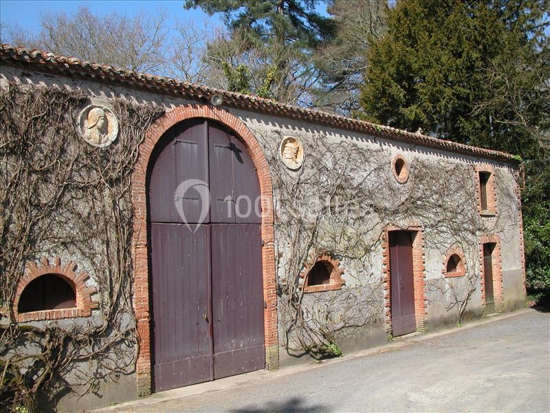 Façade d'un bâtiment ancien en pierre avec portes en bois, entouré de végétation et de branches grimpantes.