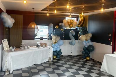 Table ronde dressée avec des verres, couverts et un centre de table en épis de blé dans un restaurant au sol carrelé.