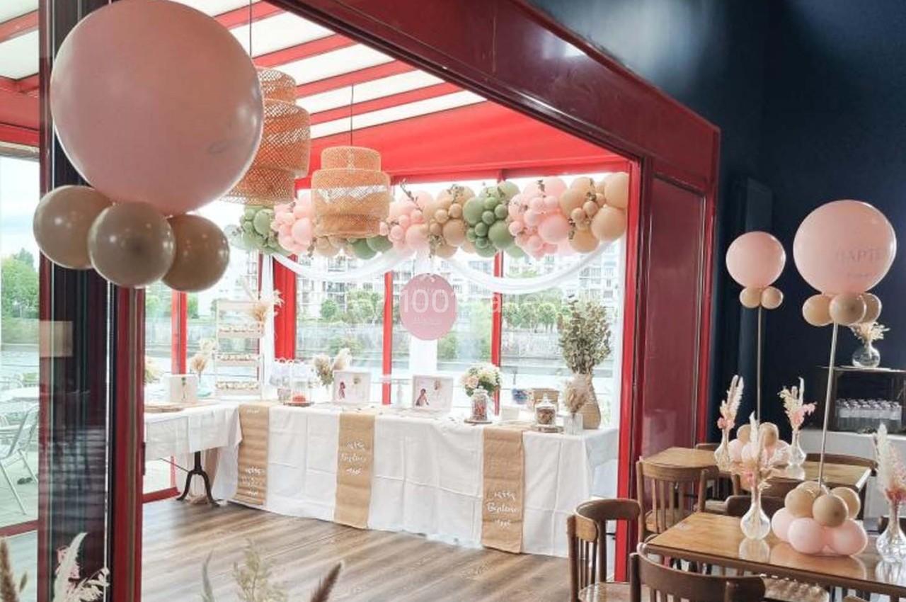 Décoration de salle avec ballons pastel et table dressée pour une réception, près de grandes baies vitrées.